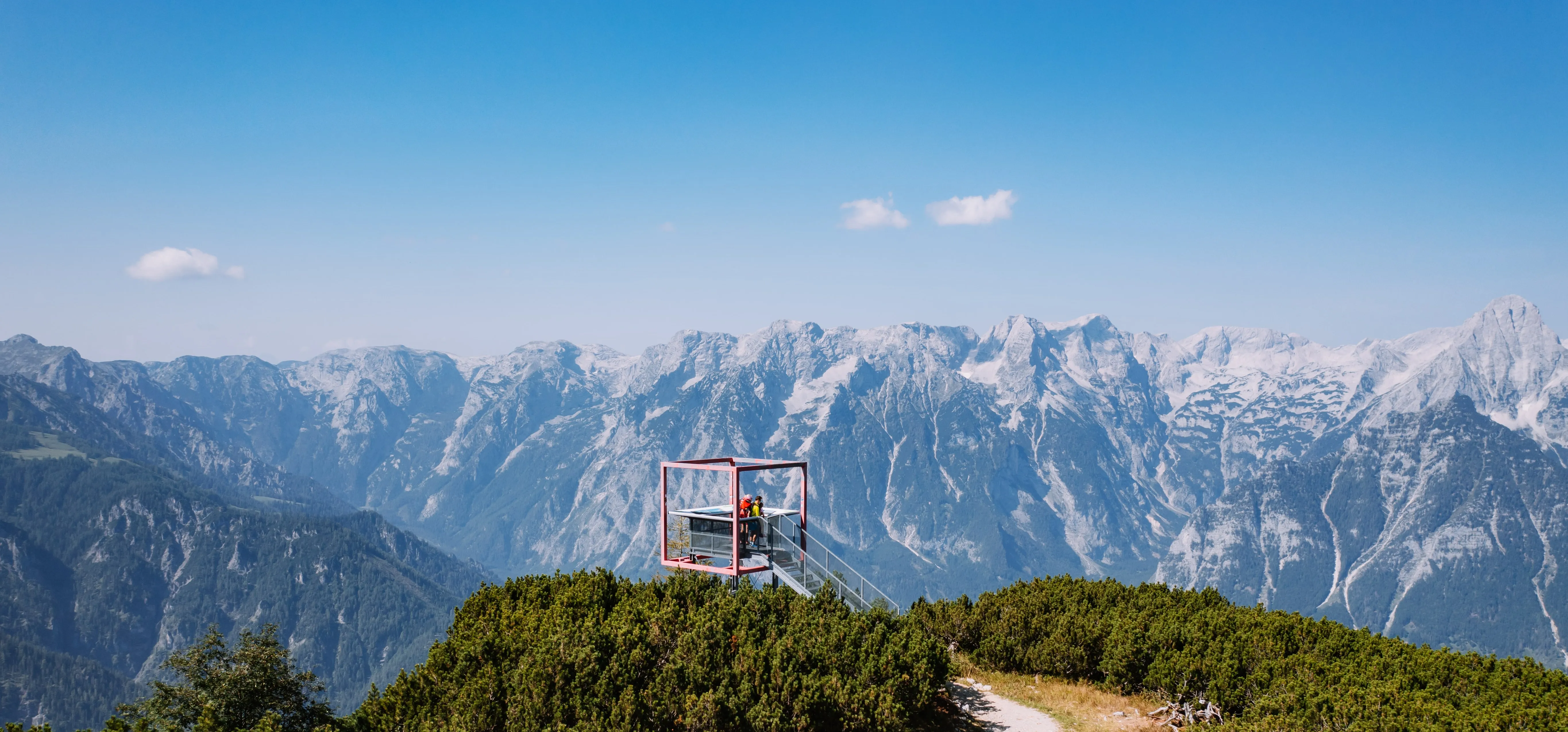 © whatifmedia / Pyhrn-Priel Tourismus GmbH Vyhlídková plošina s červeným rámem na Hössu nad Hinterstoderem, za ní vrcholy masivu Totes Gebirge
