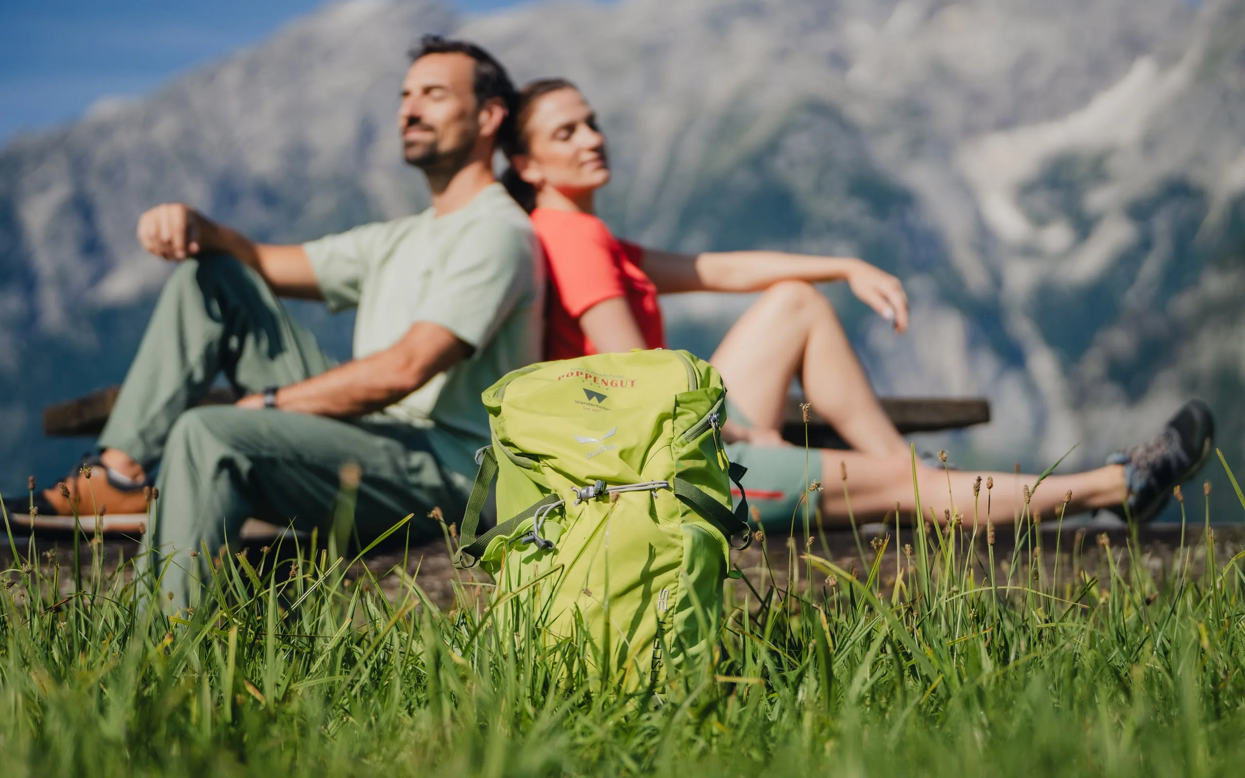 Two hikers resting on a bench in front of the mountain panorama