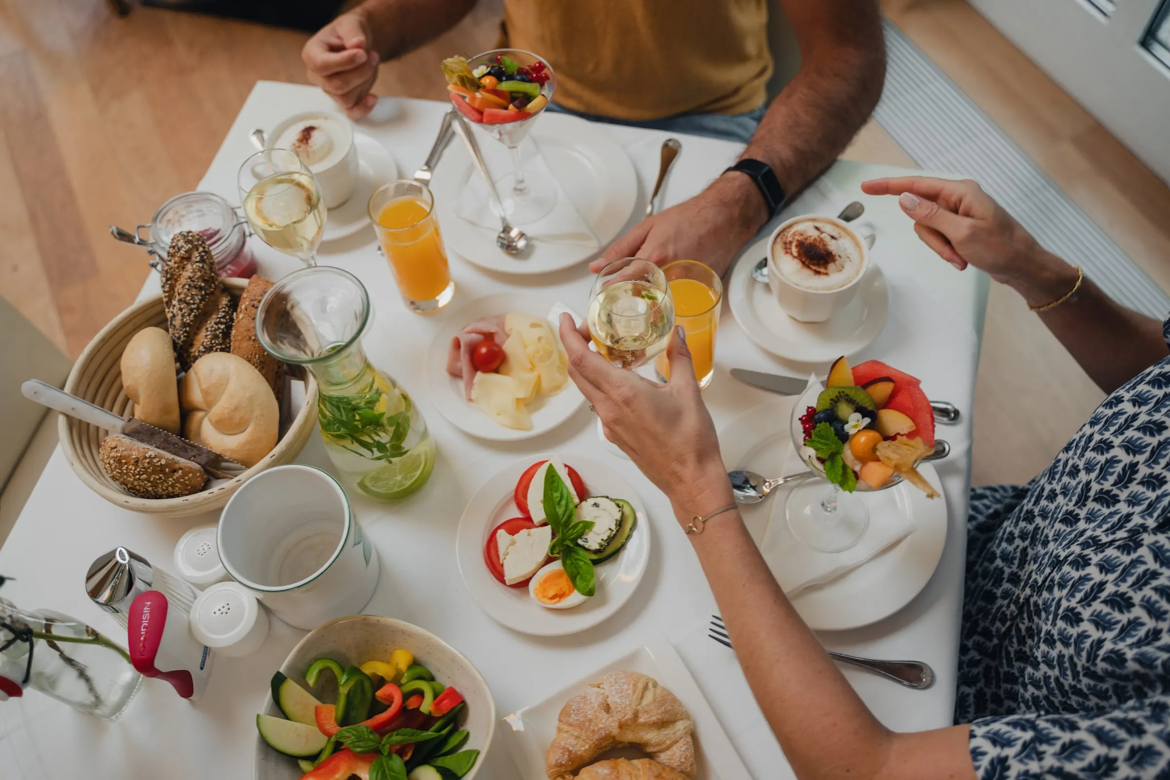 Frühstückstisch von oben mit Brotkorb, Obst, Säften und Cappuccino