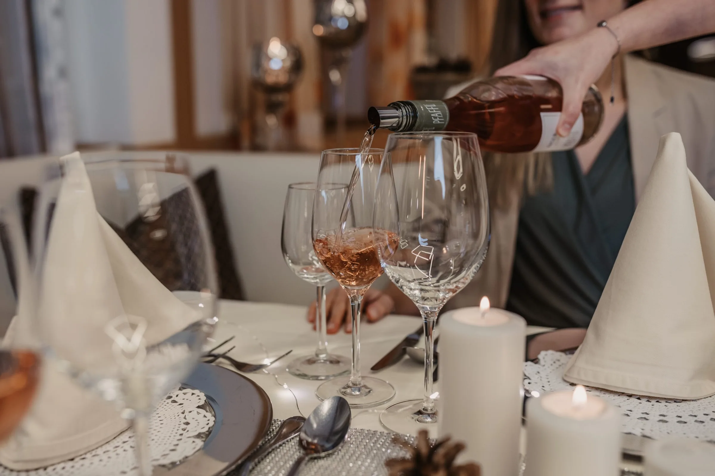 Wein wird am festlich gedeckten Tisch ins Glas eingeschenkt, daneben Kerzen und Servietten