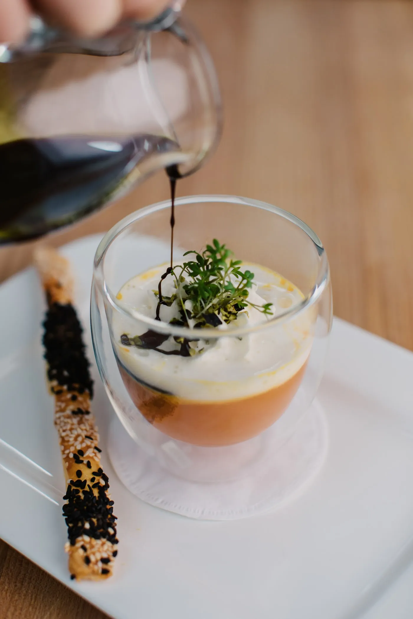 Kürbiskernöl fließt in eine Kürbiscremesuppe im Glas