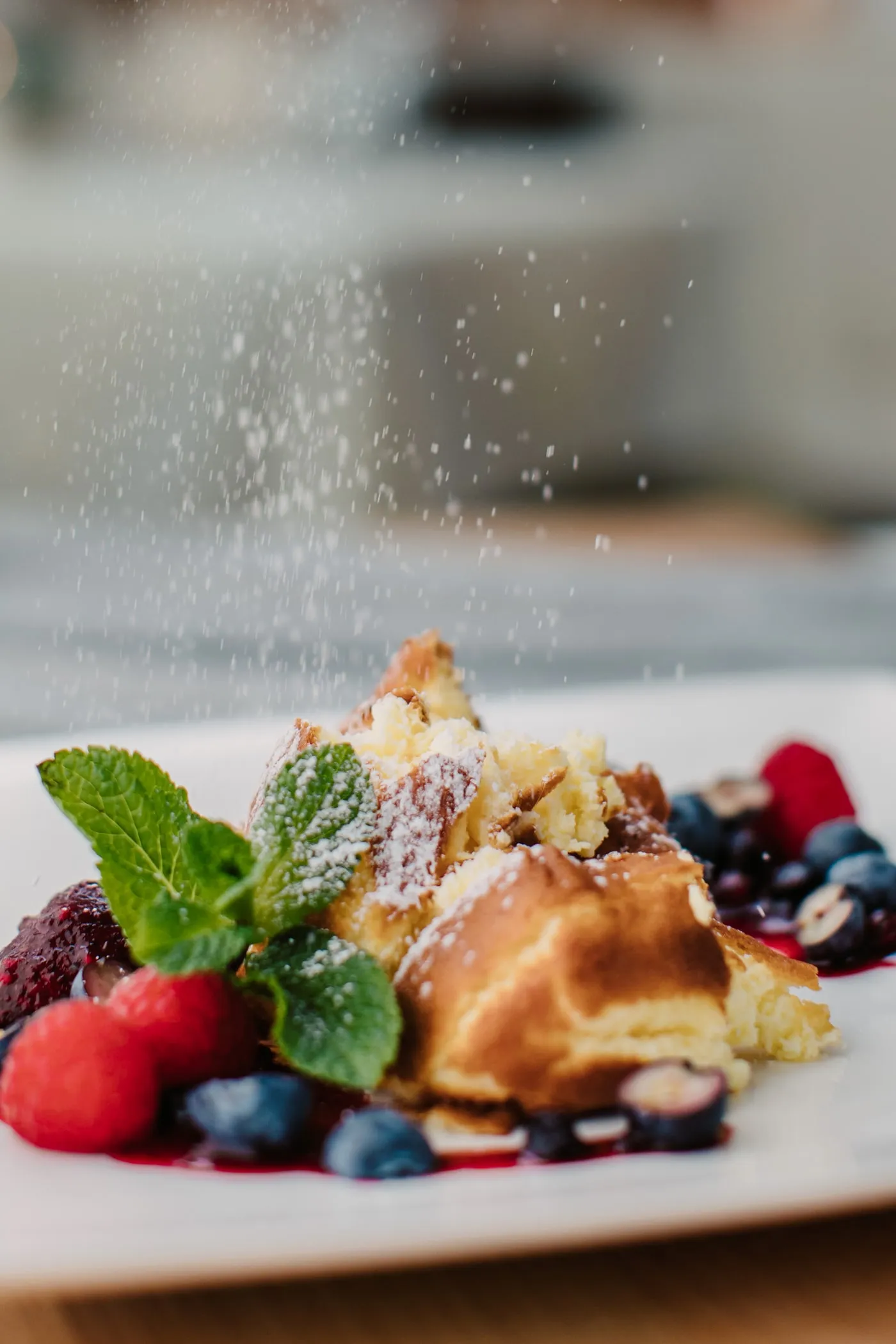 Staubzucker rieselt auf Rahmschmarrn mit Beeren