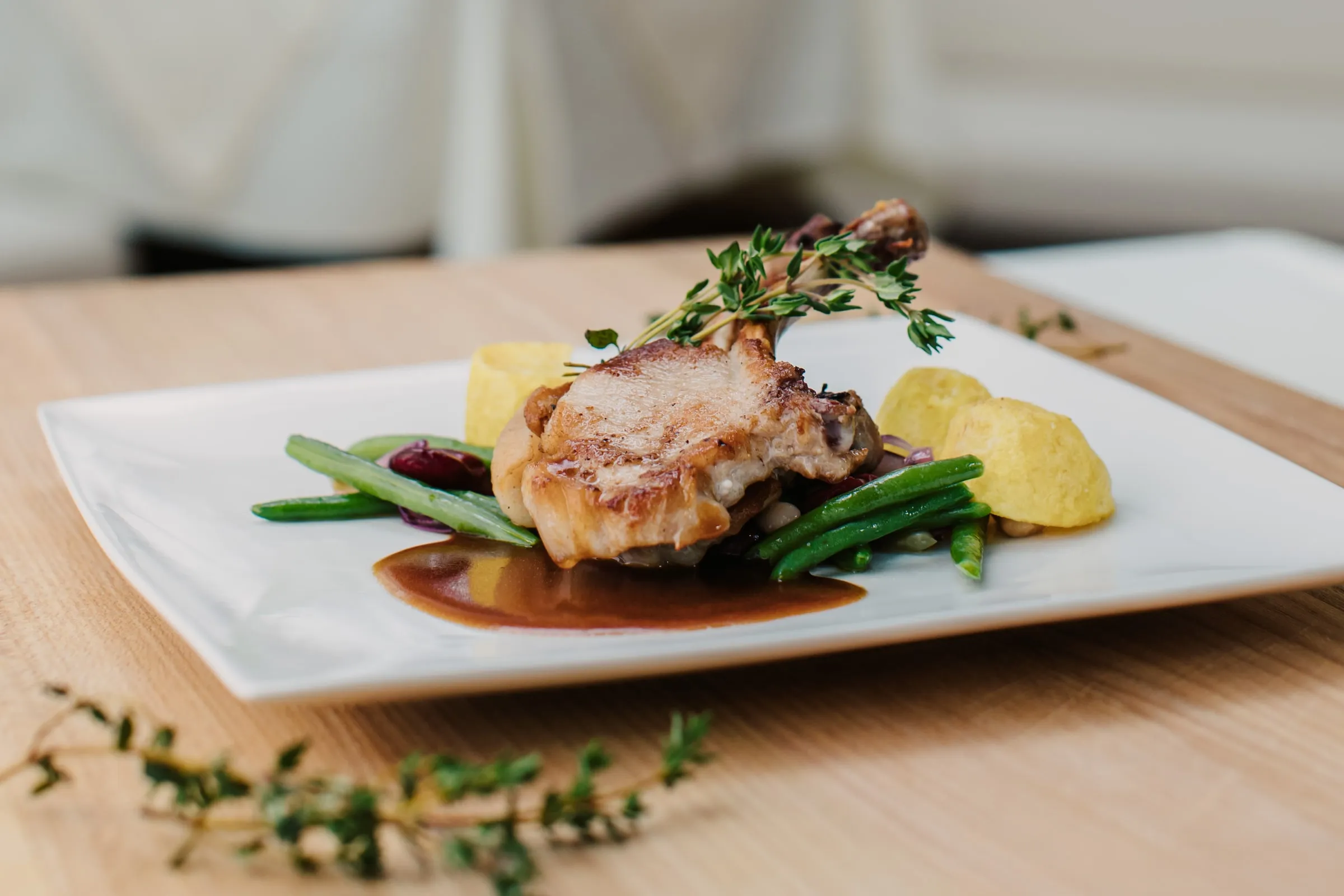 Ein angerichteter Teller mit gebratenem Fleisch, grünen Bohnen und Sauce auf einem Holztisch im Restaurant