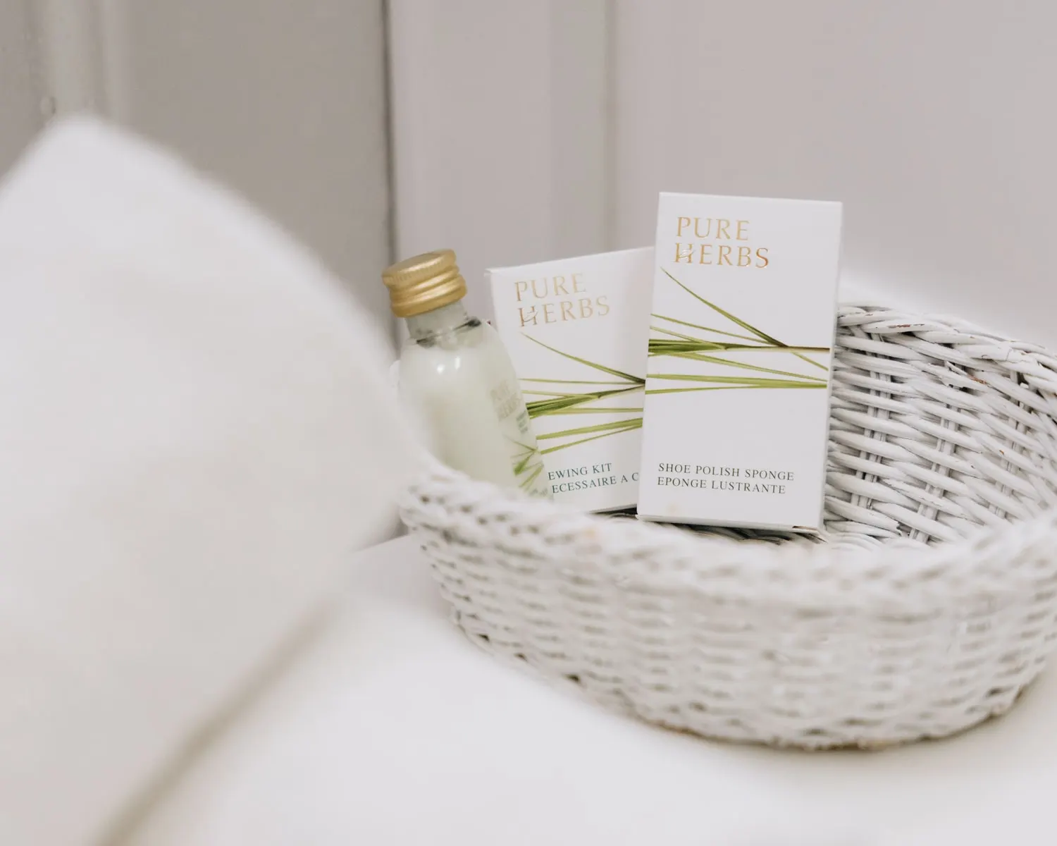 Lahvička a krabičky Pure Herbs v proutěném košíku v koupelně, vedle nich ručník