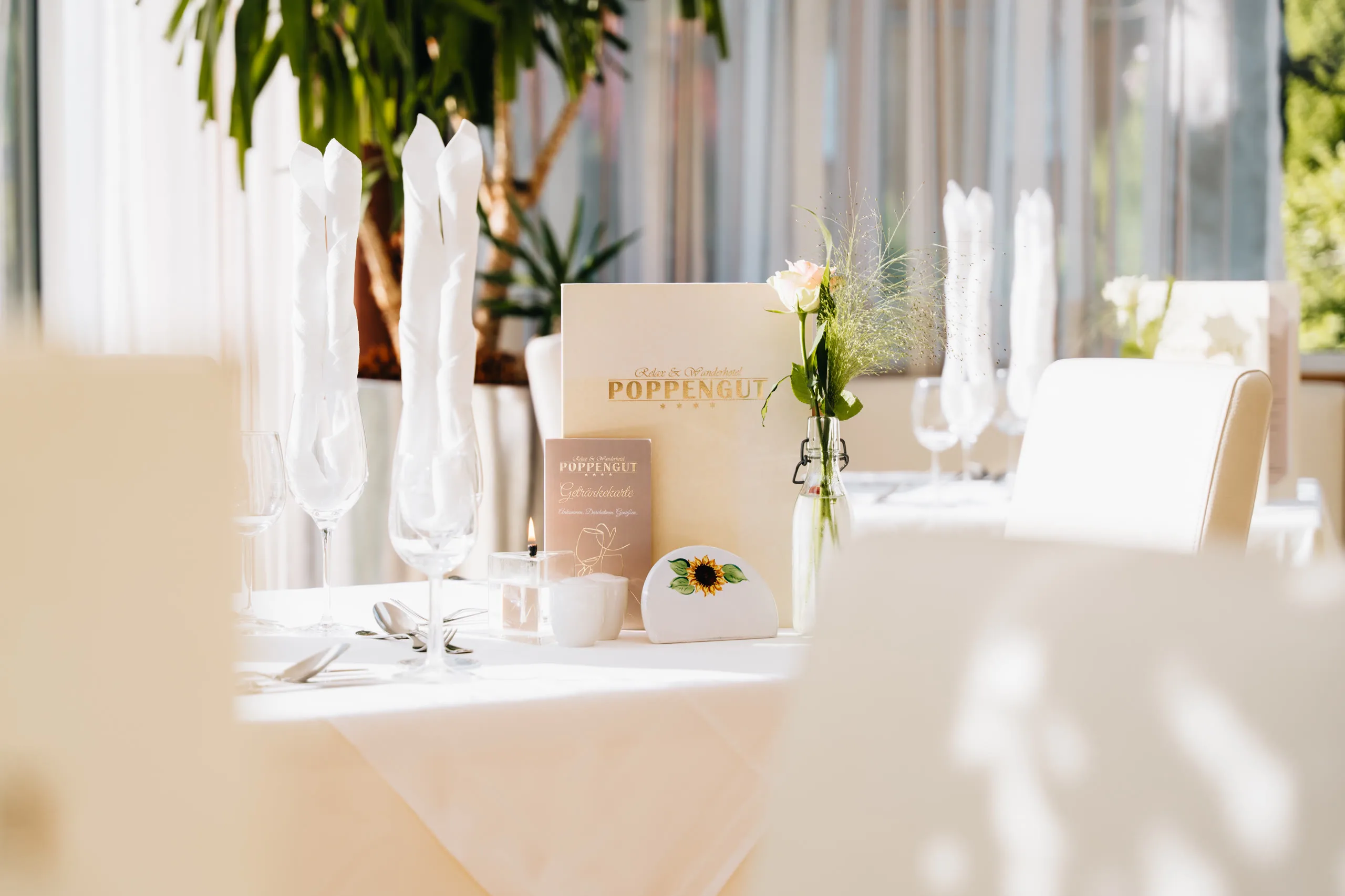 © Hartwig Winkler Slavnostně prostřený stůl v restauraci, jídelní a nápojový lístek hotelu Poppengut, svíčka a růže ve váze