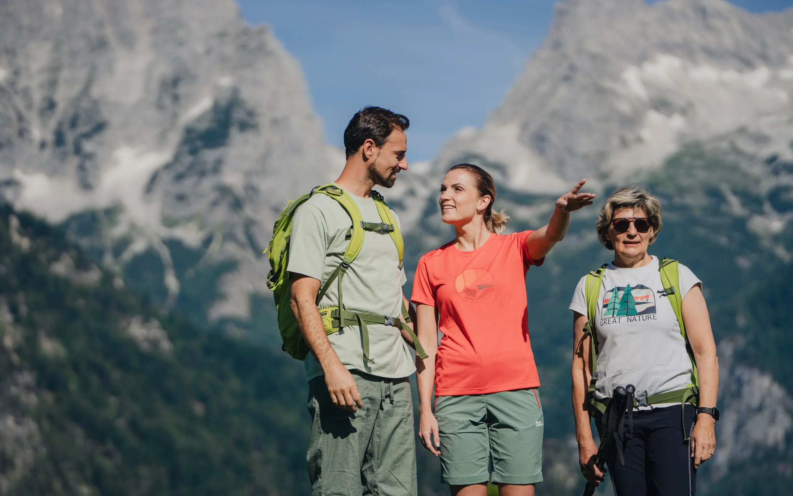 Eine Wanderführerin zeigt zwei Gästen die Gipfel