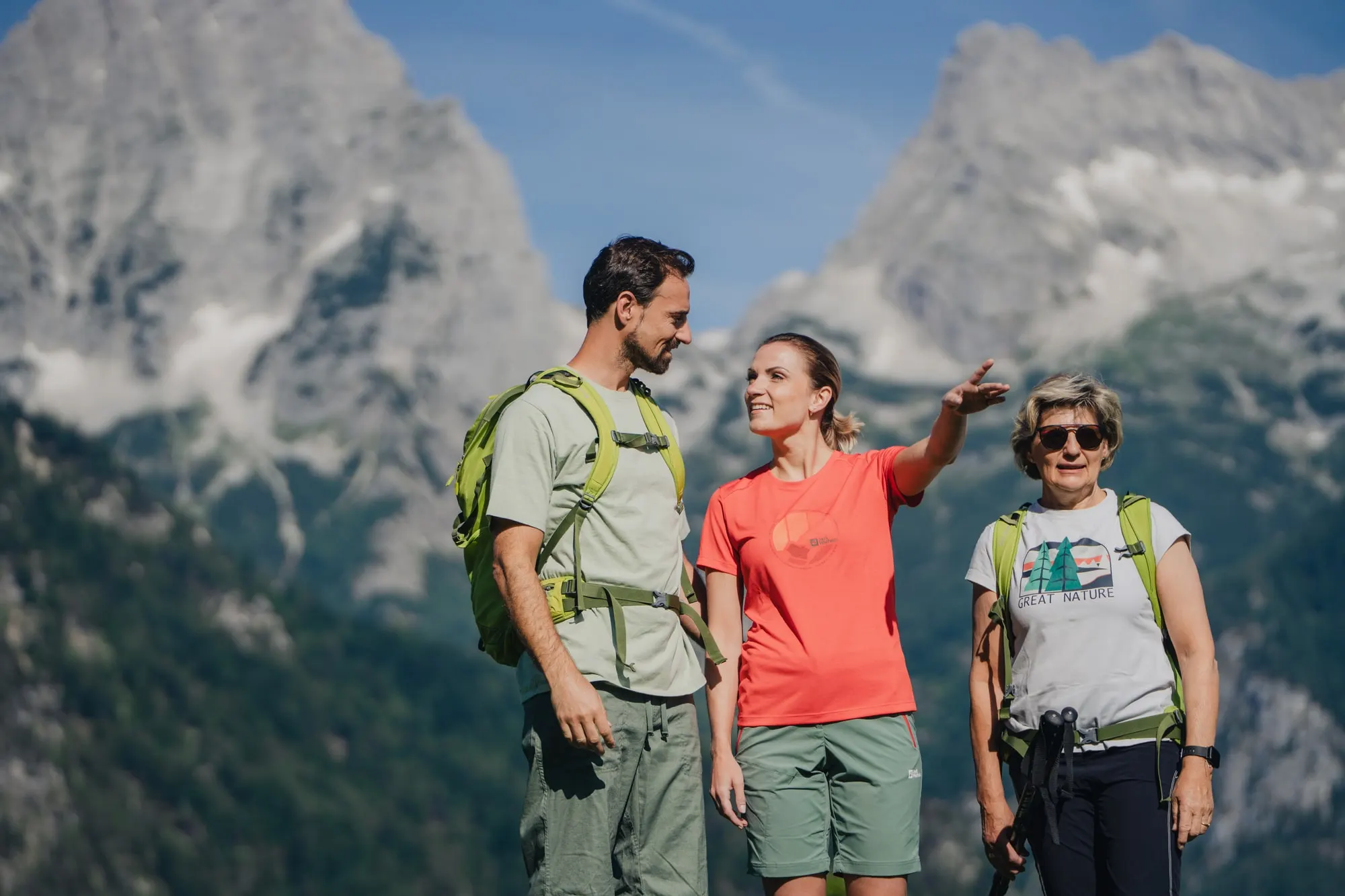 Tři turisté před skalnatými vrcholy, jedna z nich ukazuje do dálky