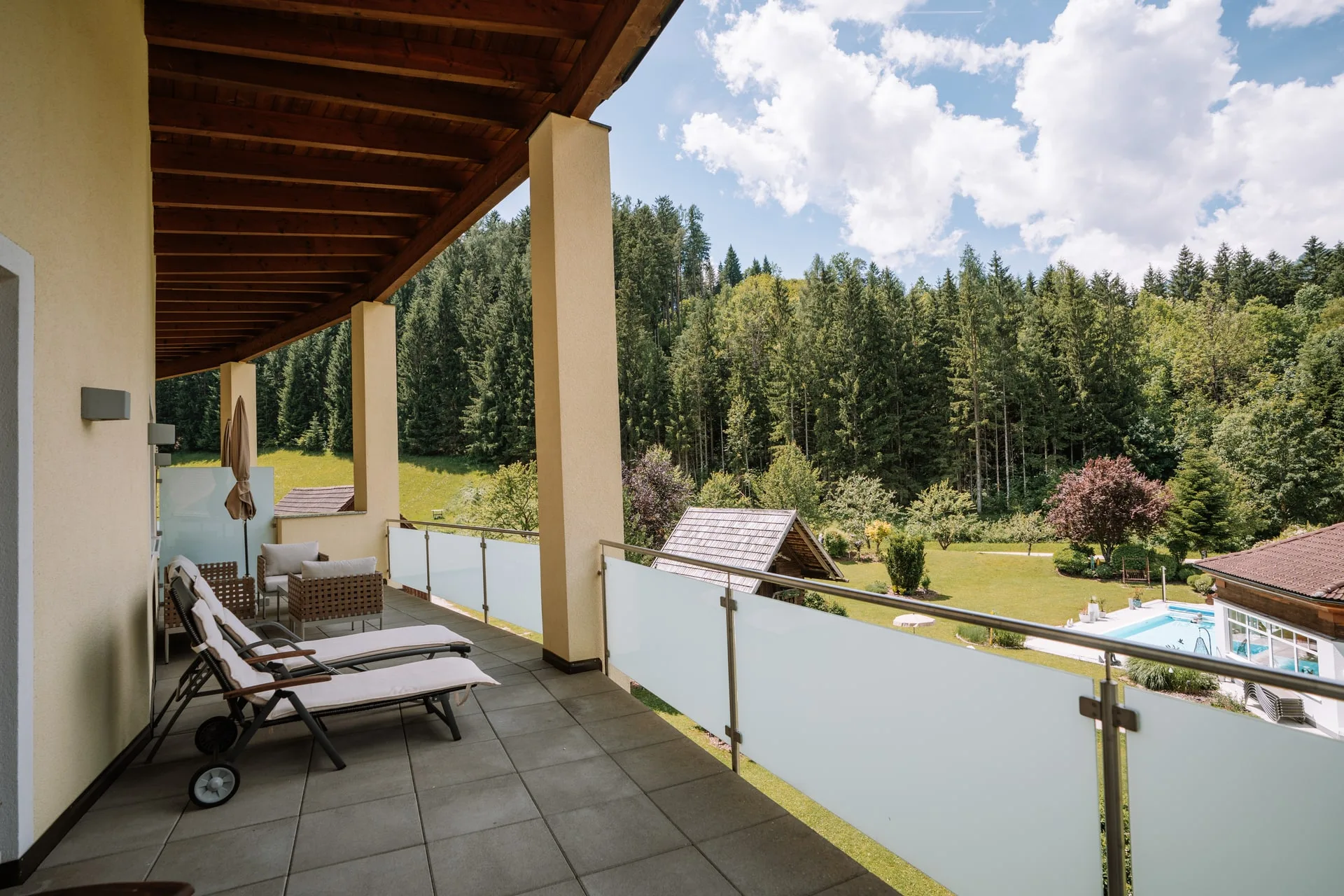 Terrasse mit Glasgeländer und Blick auf den Garten mit Pool